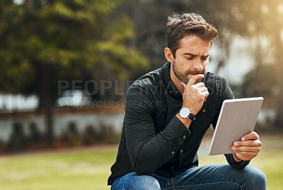 Buy stock photo Cropped shot of a handsome young man using his tablet while sitting in the park