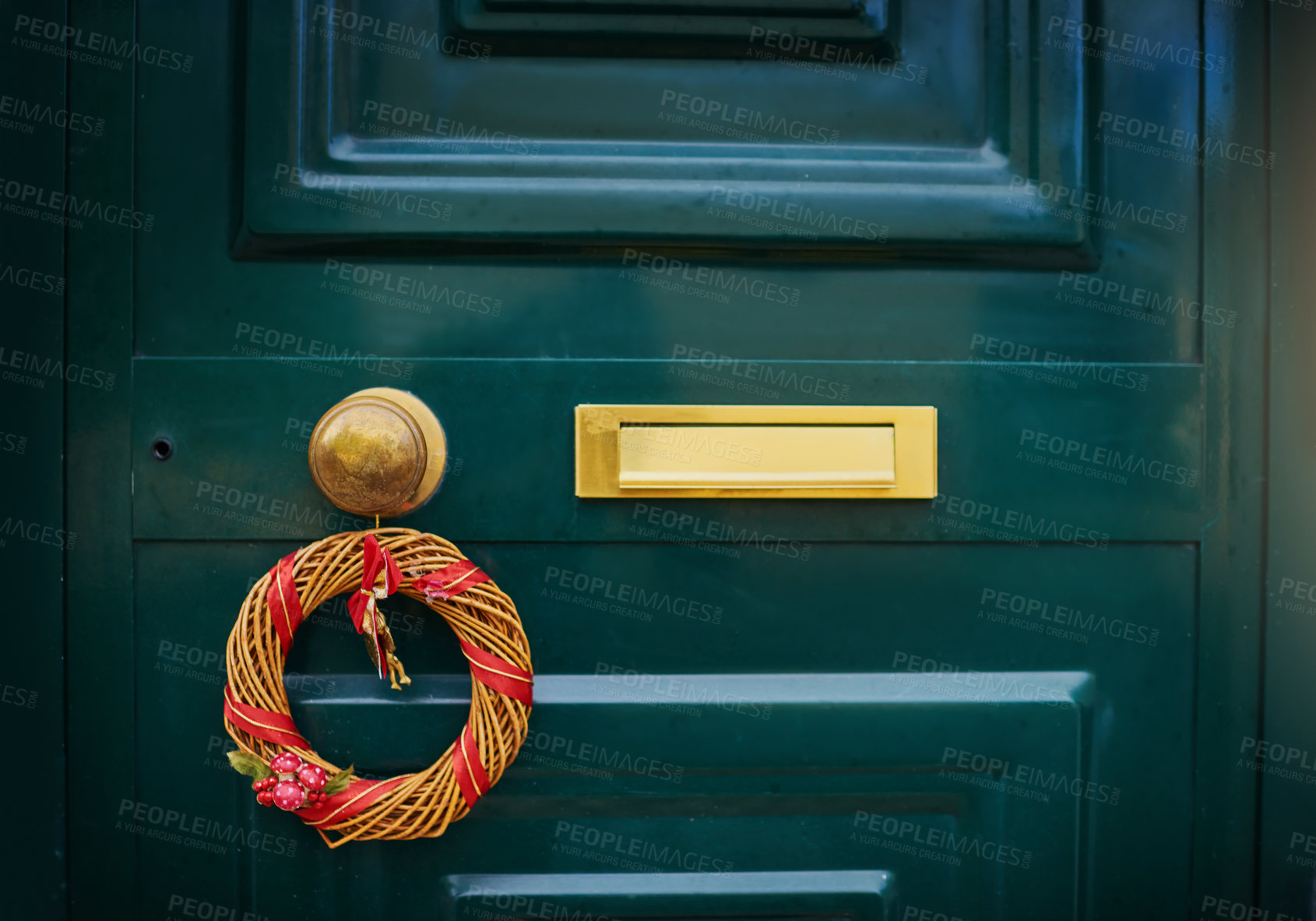 Buy stock photo Closeup of a green door with a Christmas decoration hanging on the handle outside during the day