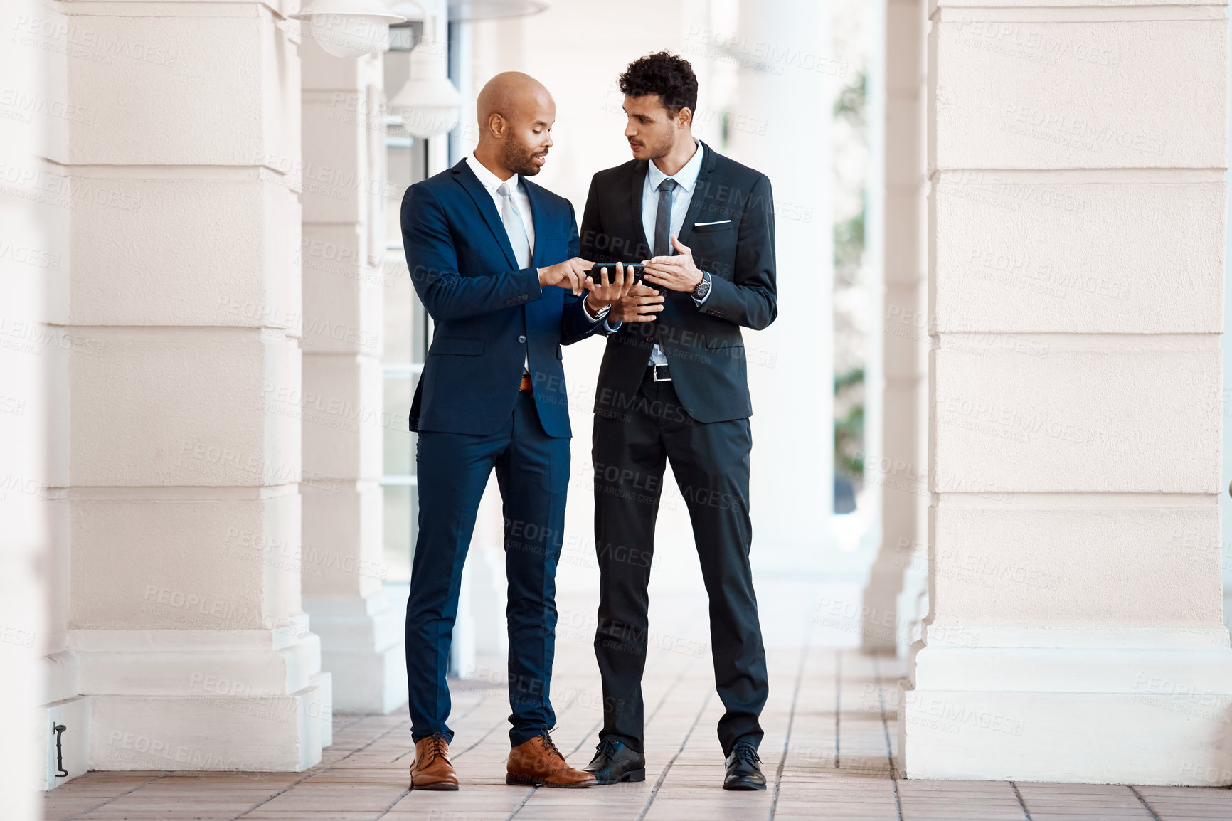 Buy stock photo Shot of young handsome businessmen using a cellphone together outside