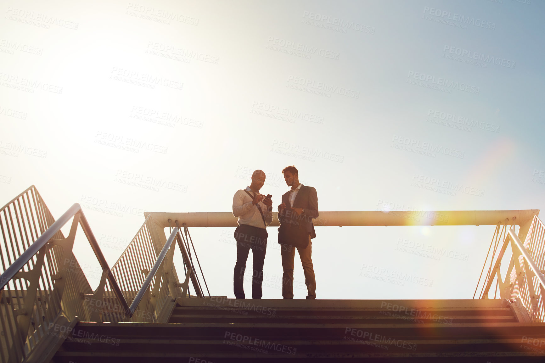 Buy stock photo Low angle shot of two businessmen using a cellphone on top of a staircase outside