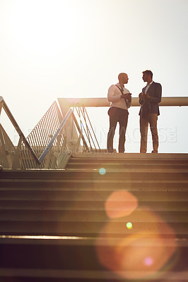 Buy stock photo Low angle shot of two businessmen using a cellphone on top of a staircase outside