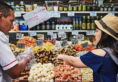 Buy stock photo Shot of a cheerful young woman browsing through a market while buying some treats from a shop owner