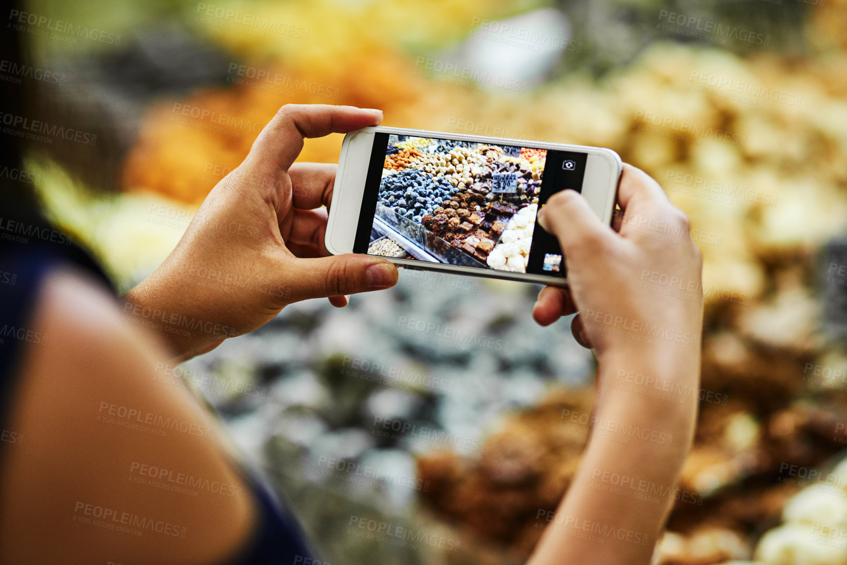 Buy stock photo Over the shoulder shot of an unrecognizable woman taking a photo of treats being sold at a market stall with her phone during the day