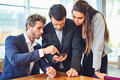Buy stock photo Cropped shot of businesspeople using a cellphone together indoors