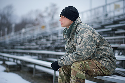 Buy stock photo Shot of a young soldier sitting outside on a snowy day at military school and looking thoughtful