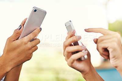 Buy stock photo Shot of a two unrecognizable women browsing and texting on their cellphones while standing inside of a cafe during the day