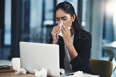 Buy stock photo Shot of a young businesswoman blowing her nose while working in an office