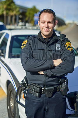 Buy stock photo Cropped portrait of a handsome young policeman standing with his arms crossed while out on patrol