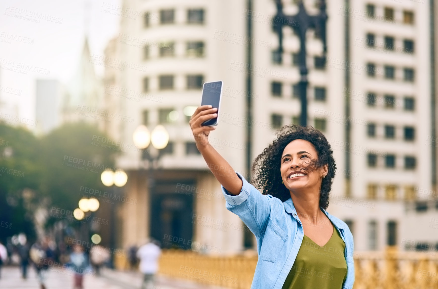 Buy stock photo Shot of a young woman taking a selfie on her cellphone while out in the city