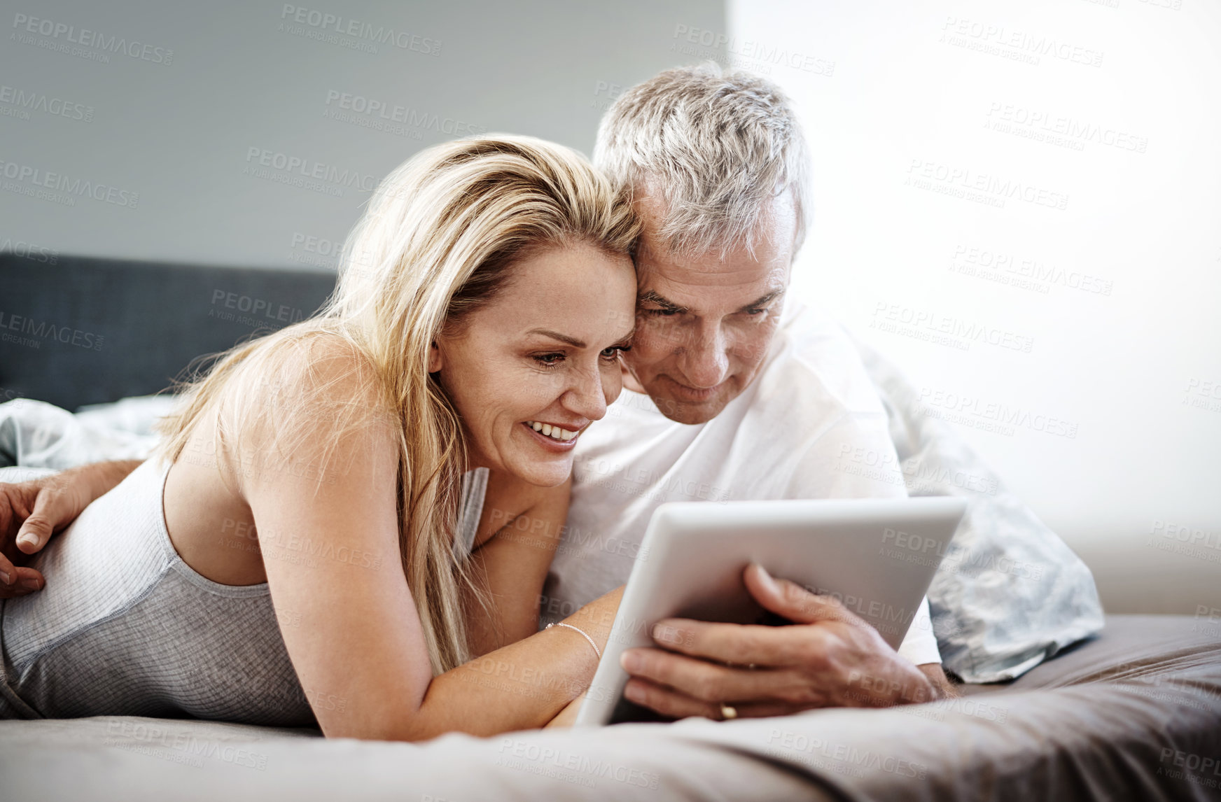 Buy stock photo Shot of a mature couple using a digital tablet while lying in bed
