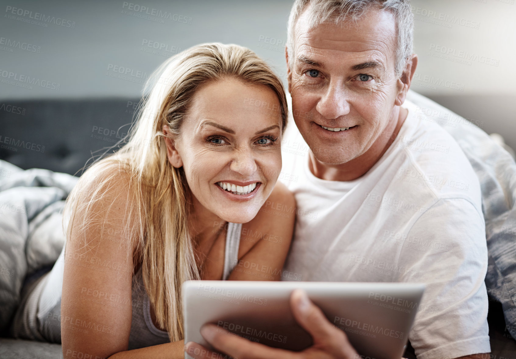 Buy stock photo Shot of a mature couple using a digital tablet while lying in bed