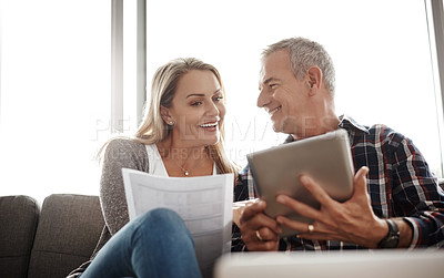 Buy stock photo Shot of a mature couple using a digital tablet while going through their paperwork together on the sofa at home