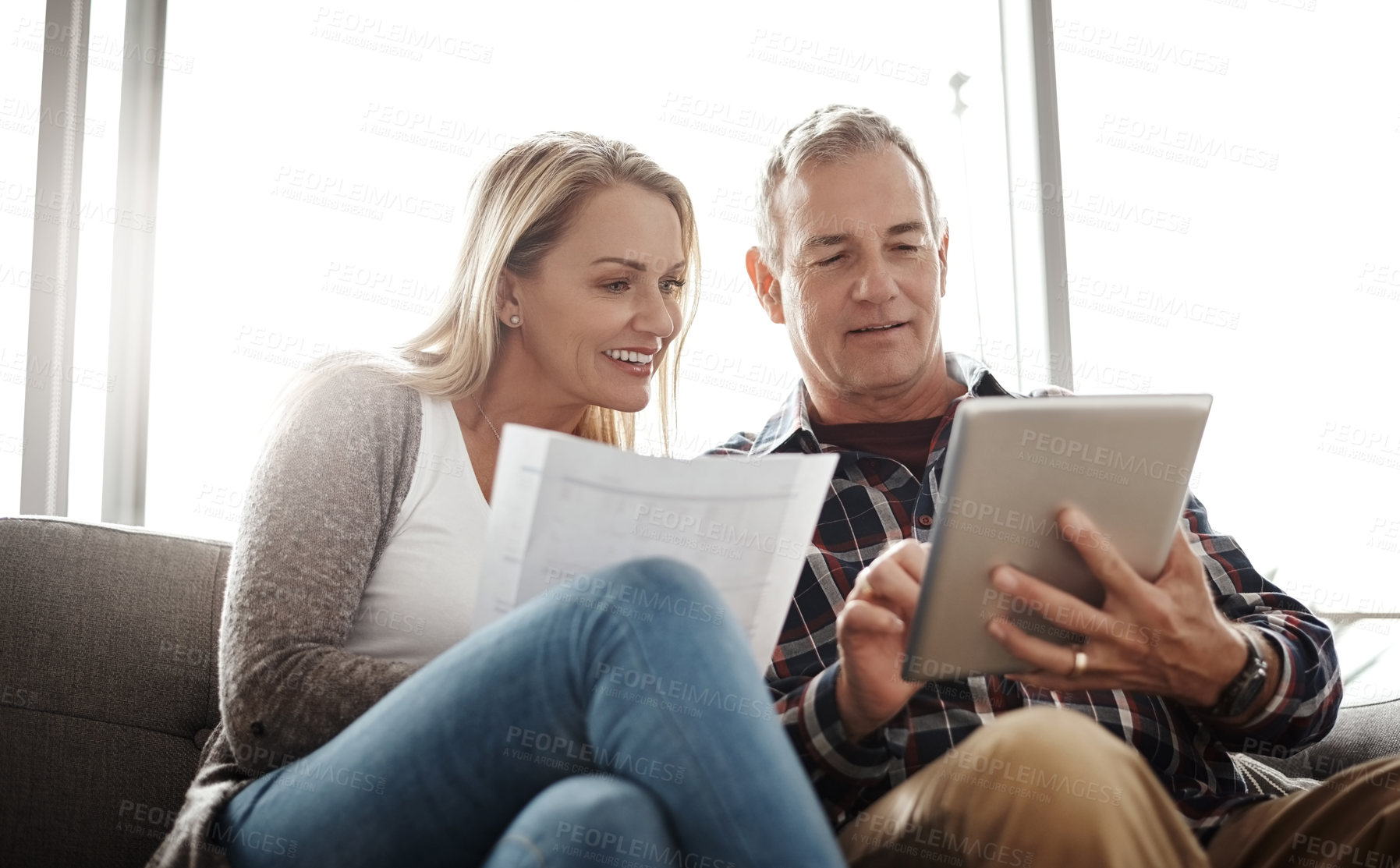 Buy stock photo Shot of a mature couple using a digital tablet while going through their paperwork together on the sofa at home