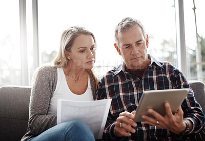 Buy stock photo Shot of a mature couple using a digital tablet while going through their paperwork together on the sofa at home