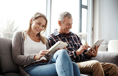 Buy stock photo Shot of a mature woman reading a book while her husband uses a digital tablet on the sofa at home
