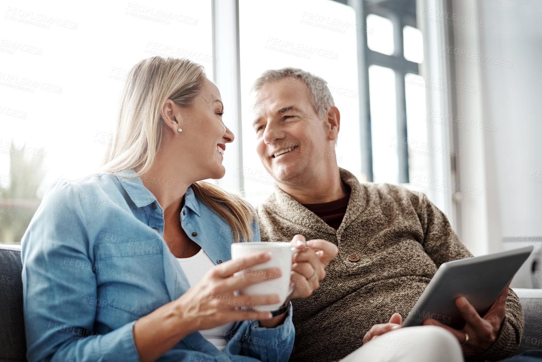 Buy stock photo Shot of a mature woman drinking coffee while her husband uses a digital tablet on the sofa at home