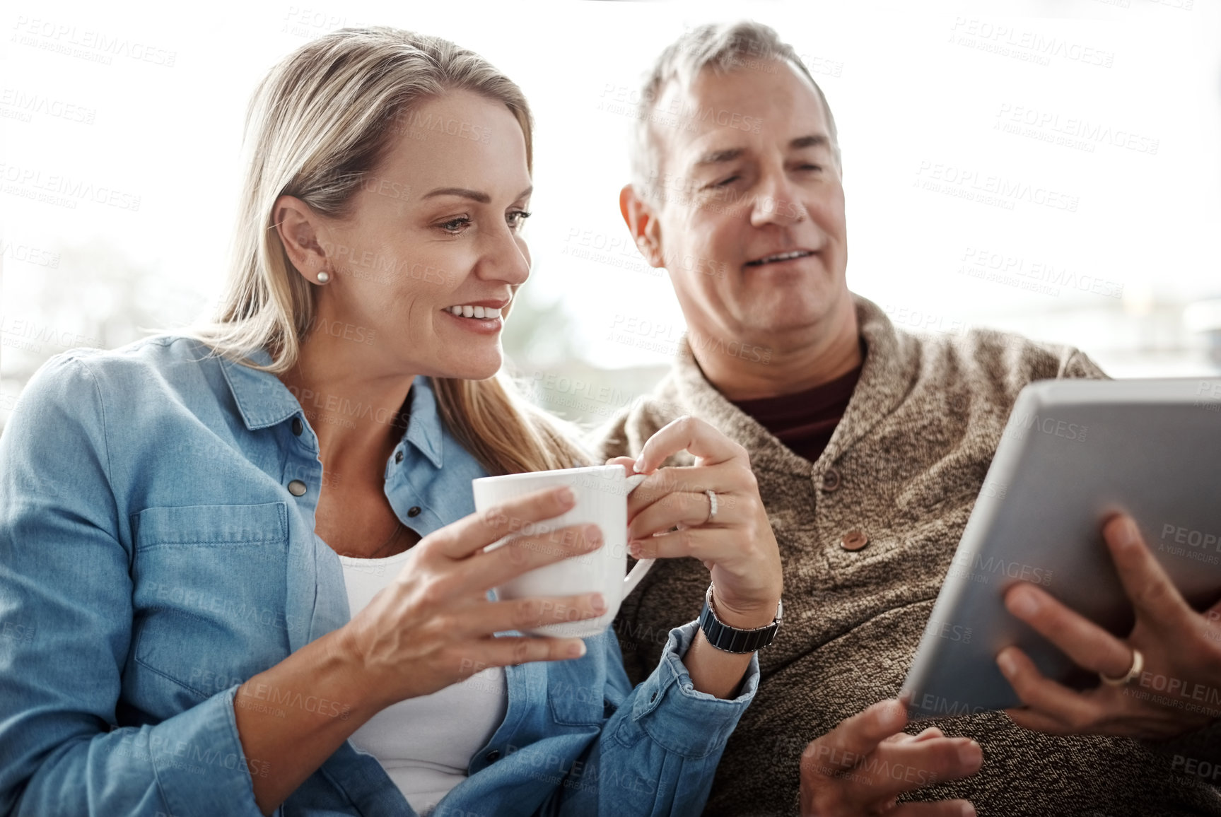 Buy stock photo Shot of a mature couple using a digital tablet while relaxing together on the sofa at home