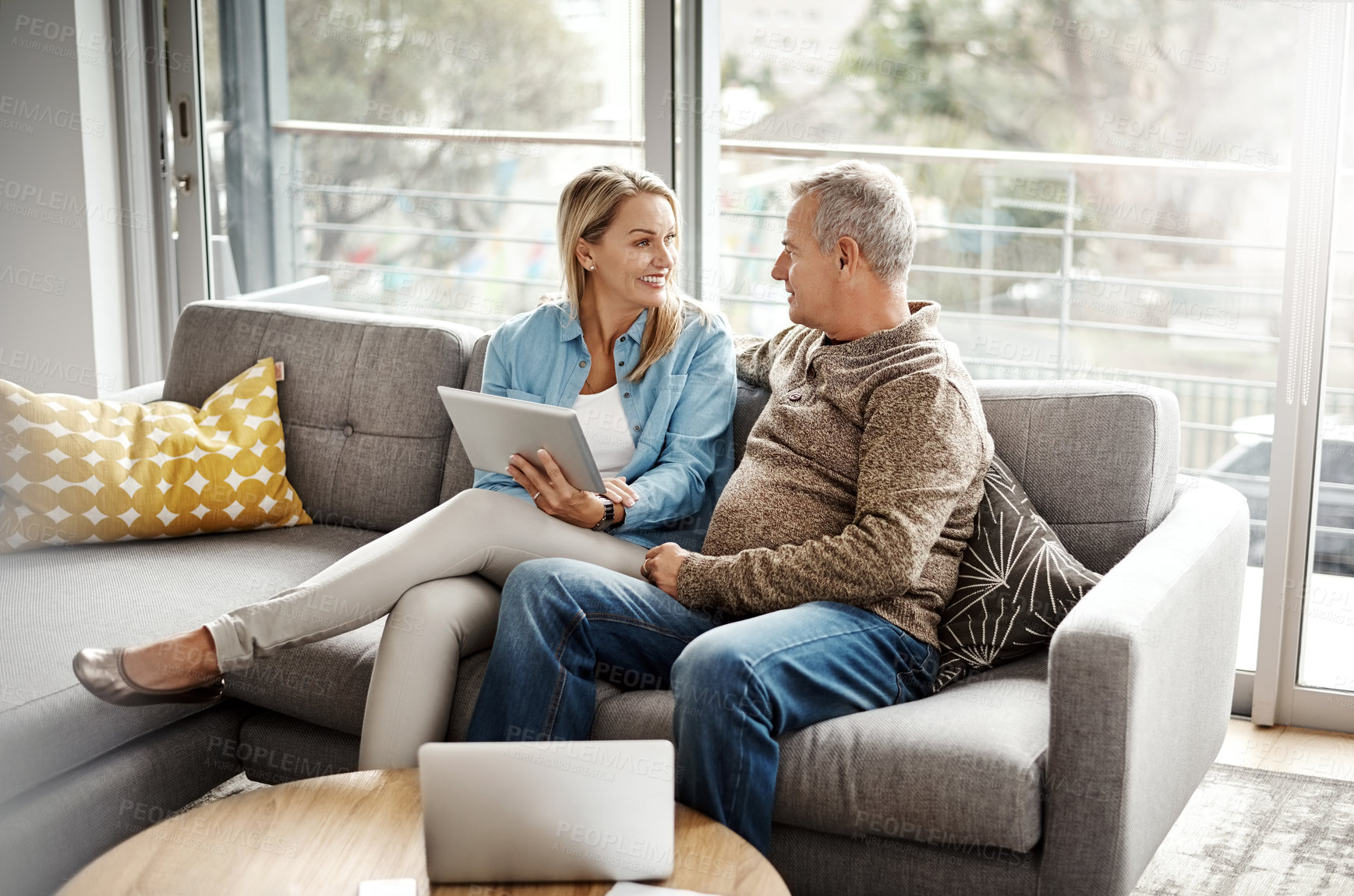 Buy stock photo Shot of a mature couple using a digital tablet while relaxing together on the sofa at home