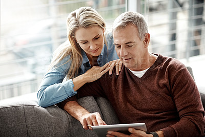 Buy stock photo Shot of a mature couple using a digital tablet while relaxing together on the sofa at home