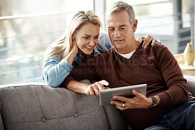 Buy stock photo Shot of a mature couple using a digital tablet while relaxing together on the sofa at home