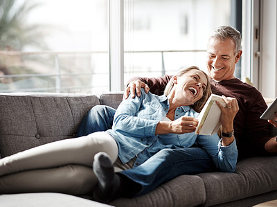 Buy stock photo Shot of a mature couple reading a book together while relaxing on the sofa at home
