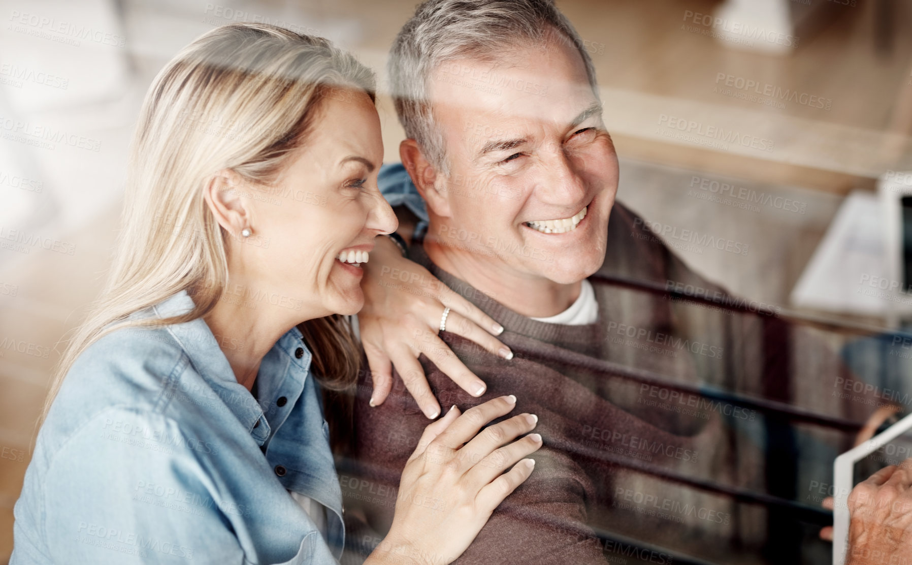 Buy stock photo Shot of a mature woman hugging her husband while he uses a digital tablet on the sofa at home
