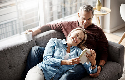 Buy stock photo Shot of a mature couple reading a book together while relaxing on the sofa at home