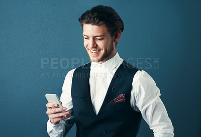Buy stock photo Studio shot of a handsome young businessman sending a text message against a blue background