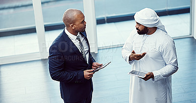 Buy stock photo Shot of two businessmen using digital tablets while having a discussion in a modern office