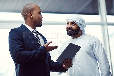 Buy stock photo Shot of two businessmen using a digital tablet while having a discussion in a modern office