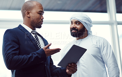 Buy stock photo Shot of two businessmen using a digital tablet while having a discussion in a modern office