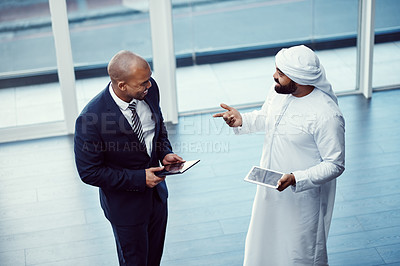 Buy stock photo Shot of two businessmen using digital tablets while having a discussion in a modern office