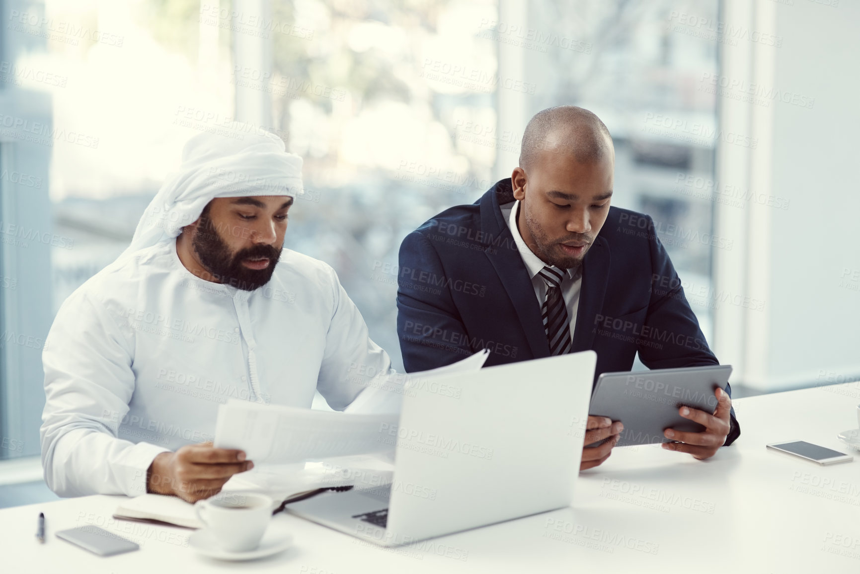 Buy stock photo Shot of two businessmen using a digital tablet and laptop while having a discussion in a modern office