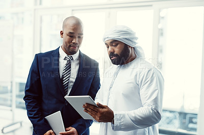 Buy stock photo Shot of two businessmen using a digital tablet while having a discussion in a modern office