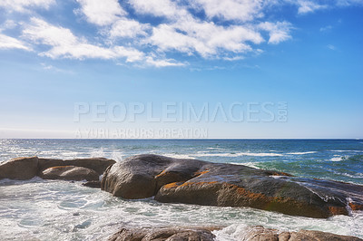Buy stock photo Landscape of large rocks in the ocean with a cloudy blue sky and copy space. Sea waves splashing against boulders on popular Camps Bay beach in Cape Town, South Africa. A beautiful summer destination