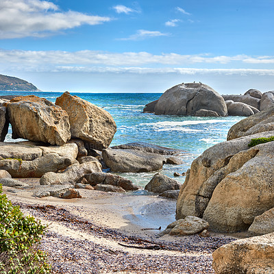 Buy stock photo Landscape of beautiful large boulders in the ocean with a blue cloudy sky. Rock or granite structures shining under the sun near calm foamy waves at a popular beach location, Cape Town, South Africa