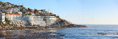 Buy stock photo Ocean view of Clifton beach in Cape Town, South Africa with blue sky and copy space. Infrastructure and houses built on a steep cliff. Calm beach and sea waves washing over rocky shoreline in summer