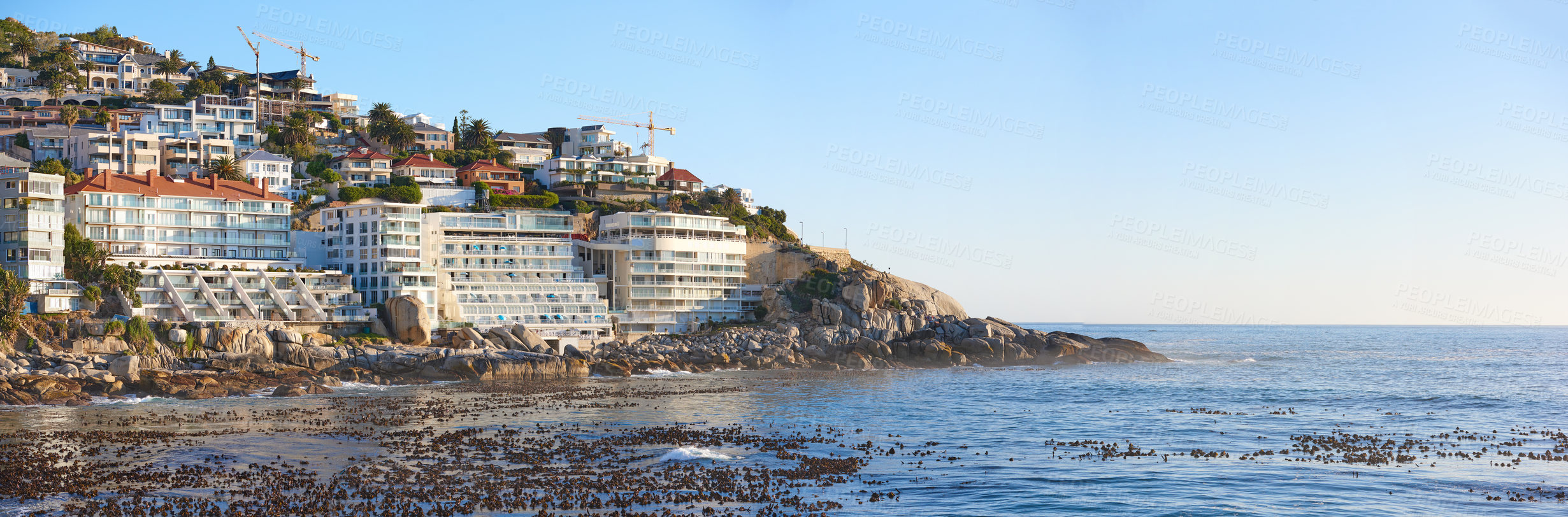 Buy stock photo Ocean view of Clifton beach in Cape Town, South Africa with blue sky and copy space. Infrastructure and houses built on a steep cliff. Calm beach and sea waves washing over rocky shoreline in summer