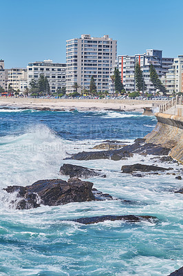Buy stock photo Rocky sea near city housing. Tall apartment buildings beside a beach on a sunny day. A popular summer vacation tourist location in South Africa. Luxury vacation resort by a blue ocean in Sea Point