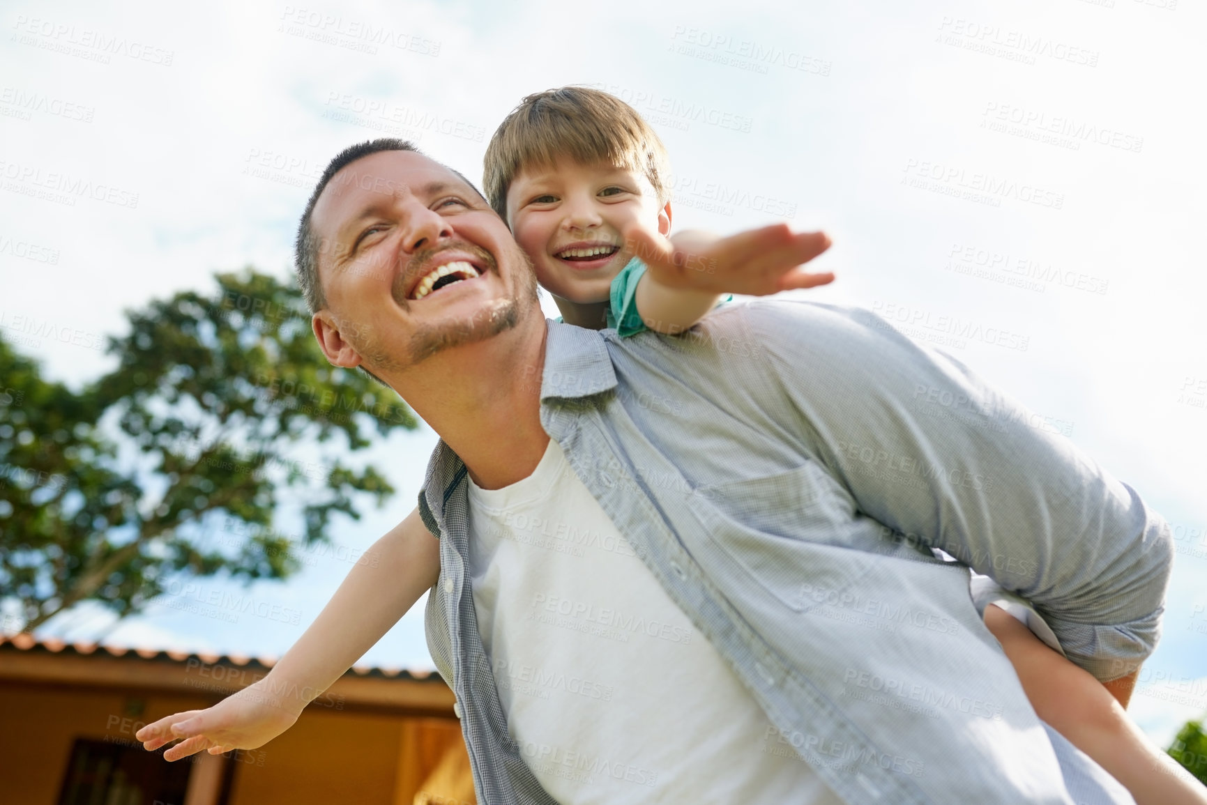 Buy stock photo Low angle shot of a young handsome father giving his adorable little son a piggyback ride in the backyard at home