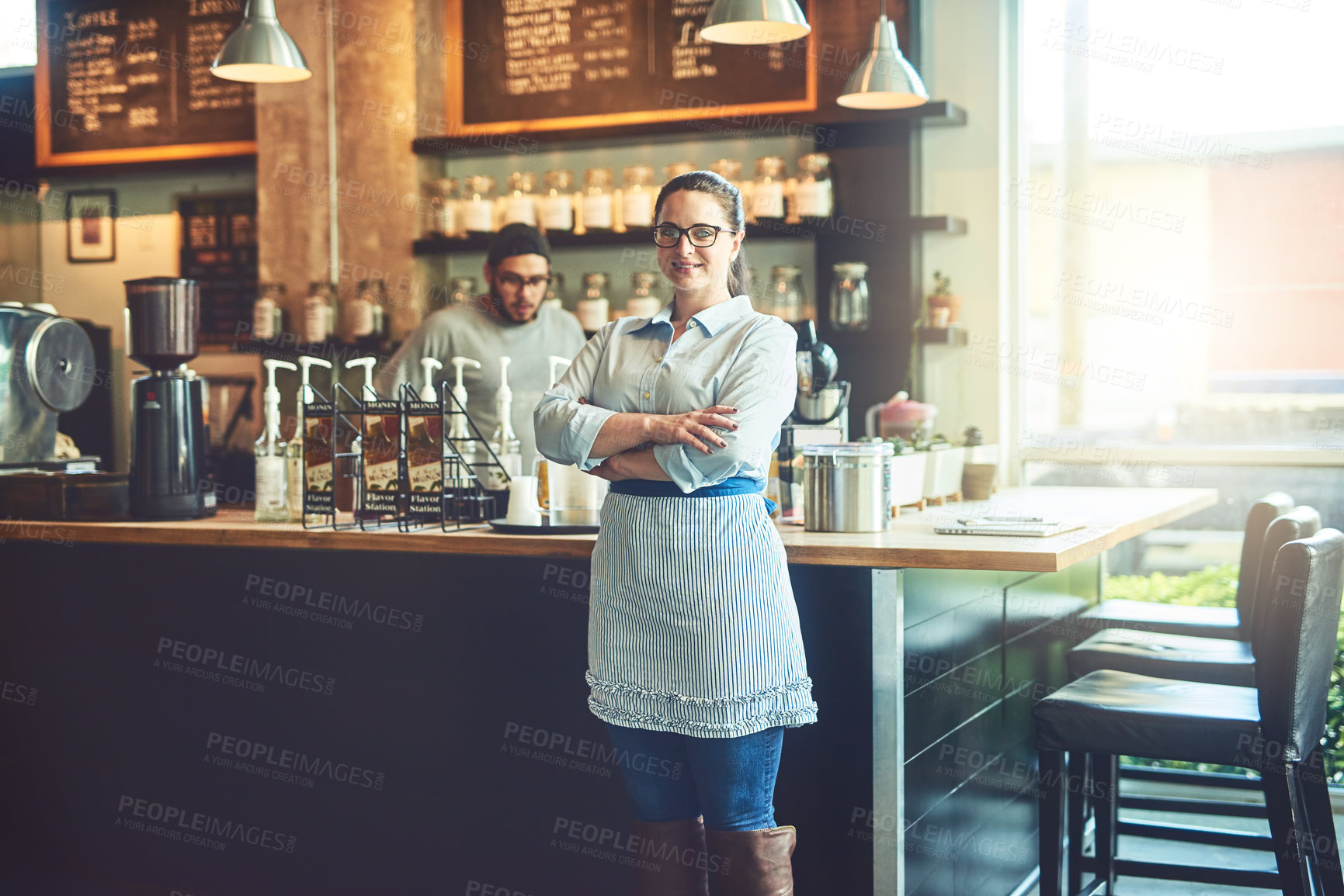 Buy stock photo Portrait of a young woman working in a cafe with her colleague in the background