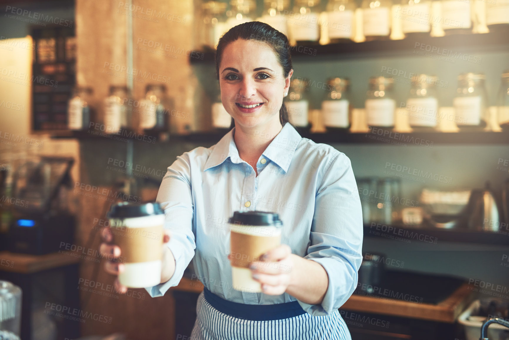 Buy stock photo Portrait of a young barista holding cups of coffee in a cafe