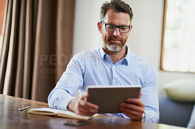 Buy stock photo Shot of a mature businessman using a digital tablet to work from home