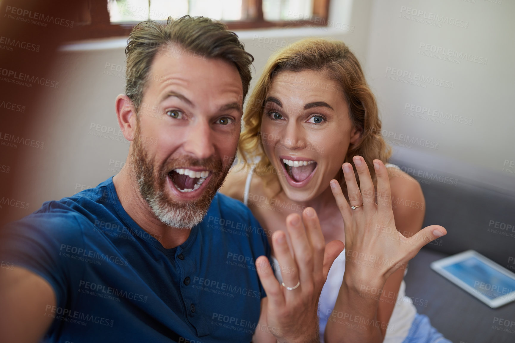 Buy stock photo Shot of a happy middle aged couple taking a selfie and showing off their wedding rings at home