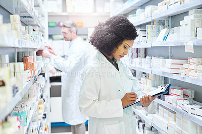 Buy stock photo Shot of a young woman doing inventory in a pharmacy with her colleague in the background