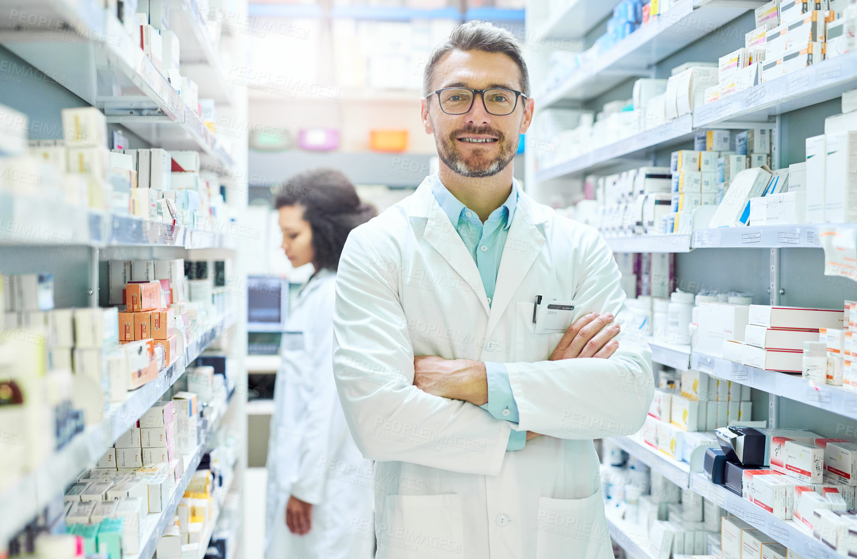 Buy stock photo Portrait of a confident mature man working in a pharmacy with his colleague in the background