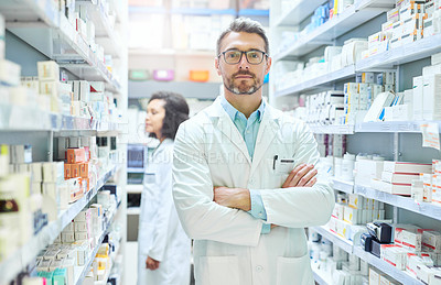 Buy stock photo Portrait of a confident mature man working in a pharmacy with his colleague in the background