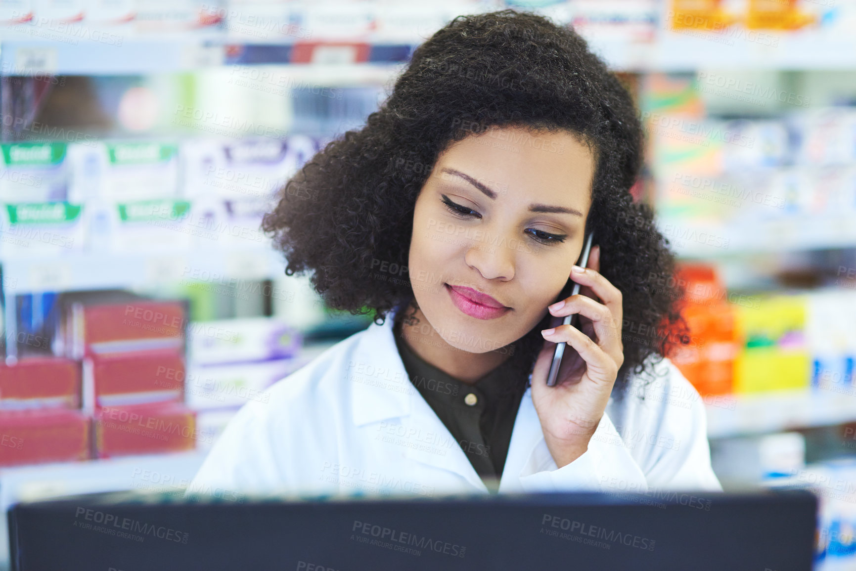 Buy stock photo Shot of a young woman using a computer and mobile phone at the counter of a pharmacy