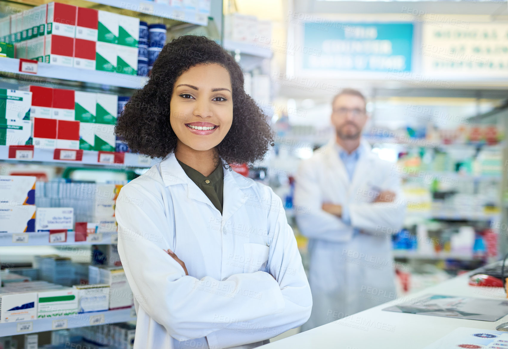 Buy stock photo Shot of a young woman working at the counter of a pharmacy with her colleague in the background