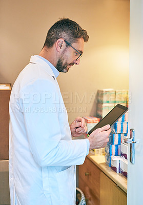 Buy stock photo Shot of a mature man using a digital tablet in the back office of a pharmacy